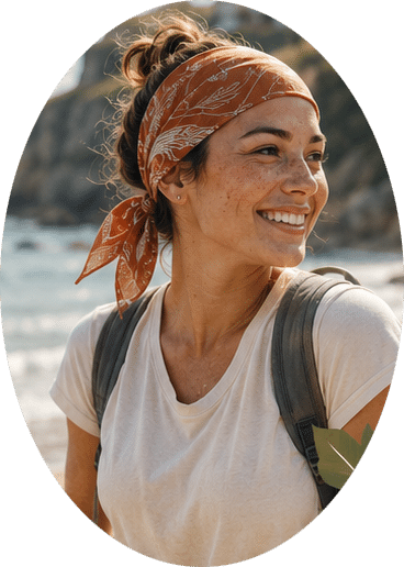 Smiling woman with an orange bandana on her head, white t-shirt, and backpack at the beach with ocean in the background